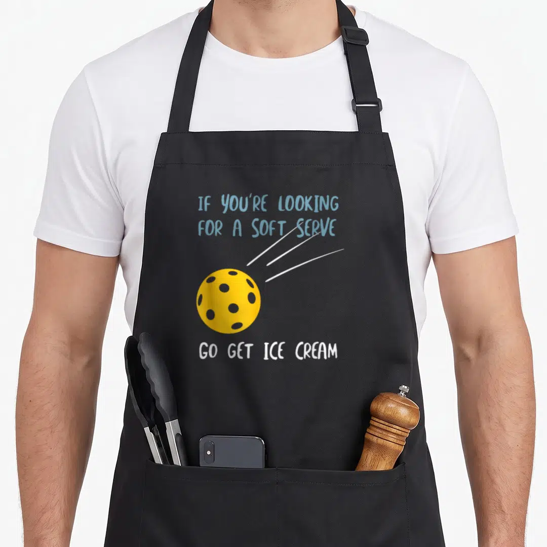 Pun pickleball apron - Yellow pickleball with white motion lines under blue text and white text below — shown on a black cotton canvas apron against a white background