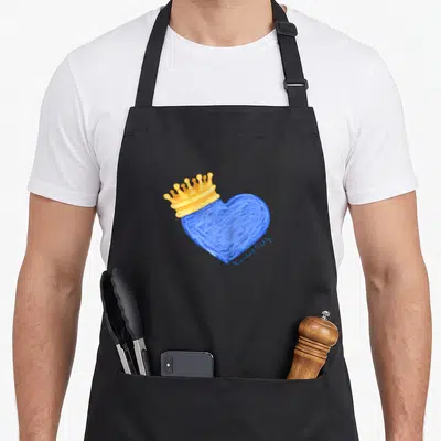 Kansas crown royal apron - Blue heart illustration topped with a gold crown and small script reading Kansas City — shown on a black cotton canvas apron against a white background