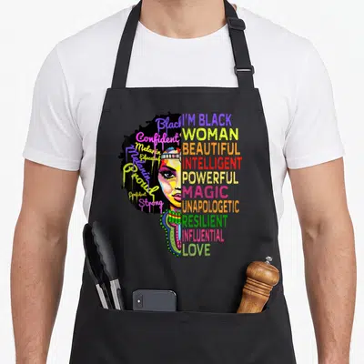 Juneteenth history african apron - Split-face woman with dripping script and stacked block words in black yellow pink — shown on a black cotton canvas apron against a white background