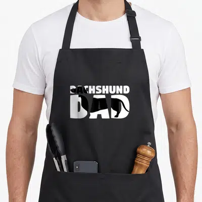 Dach wiener apron - DACHSHUND DAD text with black dachshund silhouette inside white letters — shown on a black cotton canvas apron against a white background
