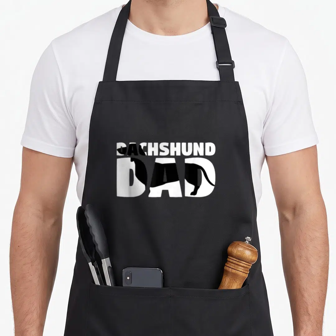 Dach wiener apron - DACHSHUND DAD text with black dachshund silhouette inside white letters — shown on a black cotton canvas apron against a white background