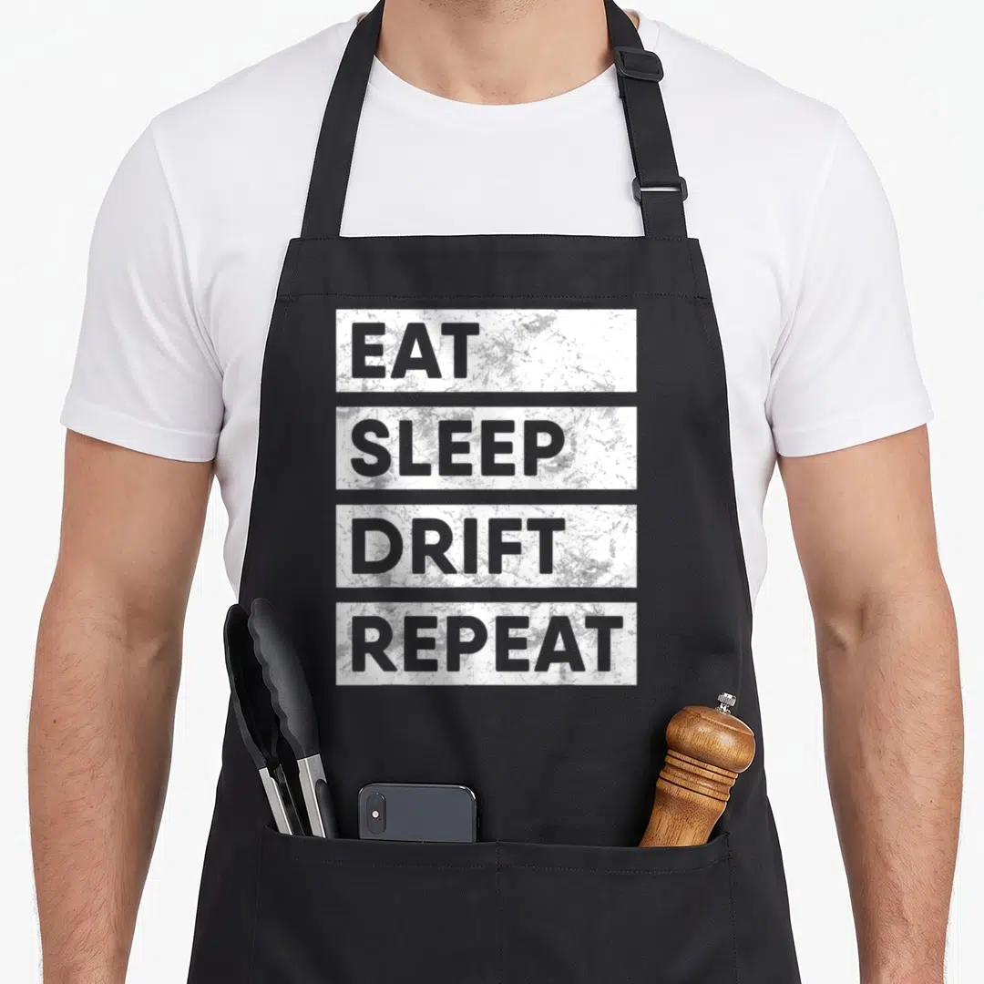 Sleep car apron - Four stacked white distressed blocks with grey text reading Eat Sleep Drift Repeat — shown on a black cotton canvas apron against a white background