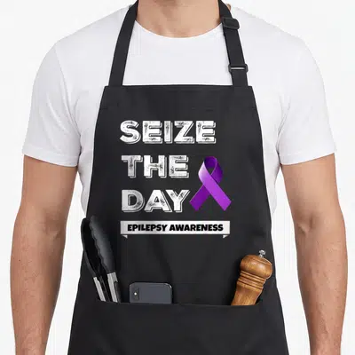 Seize epilepsy awareness apron - Distressed white SEIZE THE DAY text next to purple ribbon above EPILEPSY AWARENESS — shown on a black cotton canvas apron against a white background