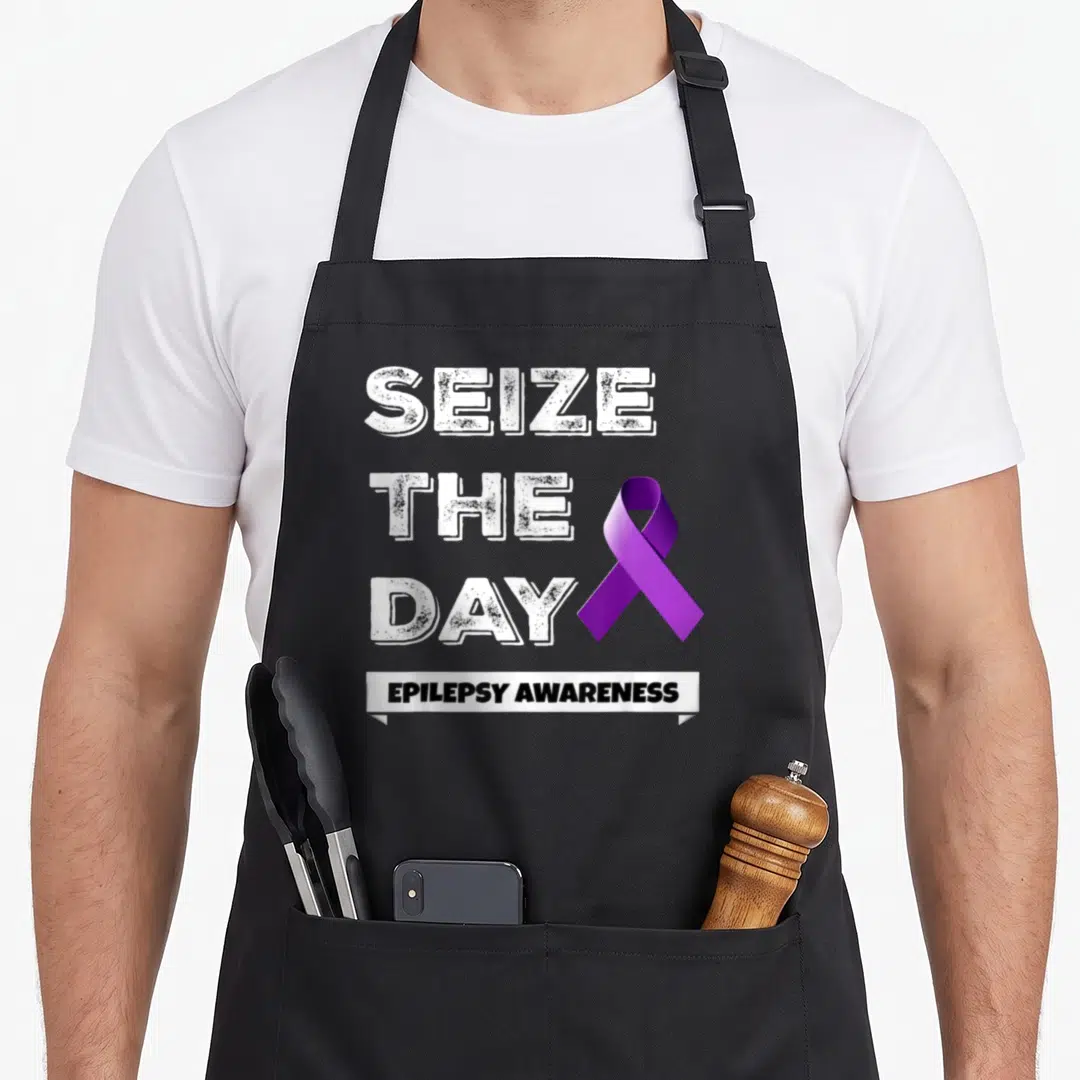 Seize epilepsy awareness apron - Distressed white SEIZE THE DAY text next to purple ribbon above EPILEPSY AWARENESS — shown on a black cotton canvas apron against a white background