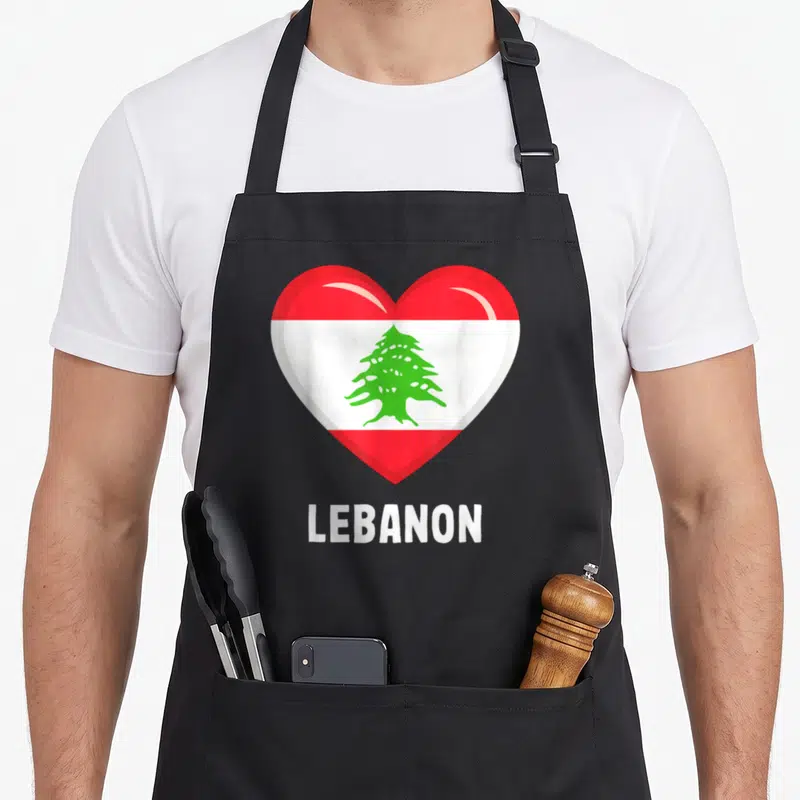 Lebanon flag lebanese apron - Red white and green heart with green cedar tree above white LEBANON text — shown on a black cotton canvas apron against a white background
