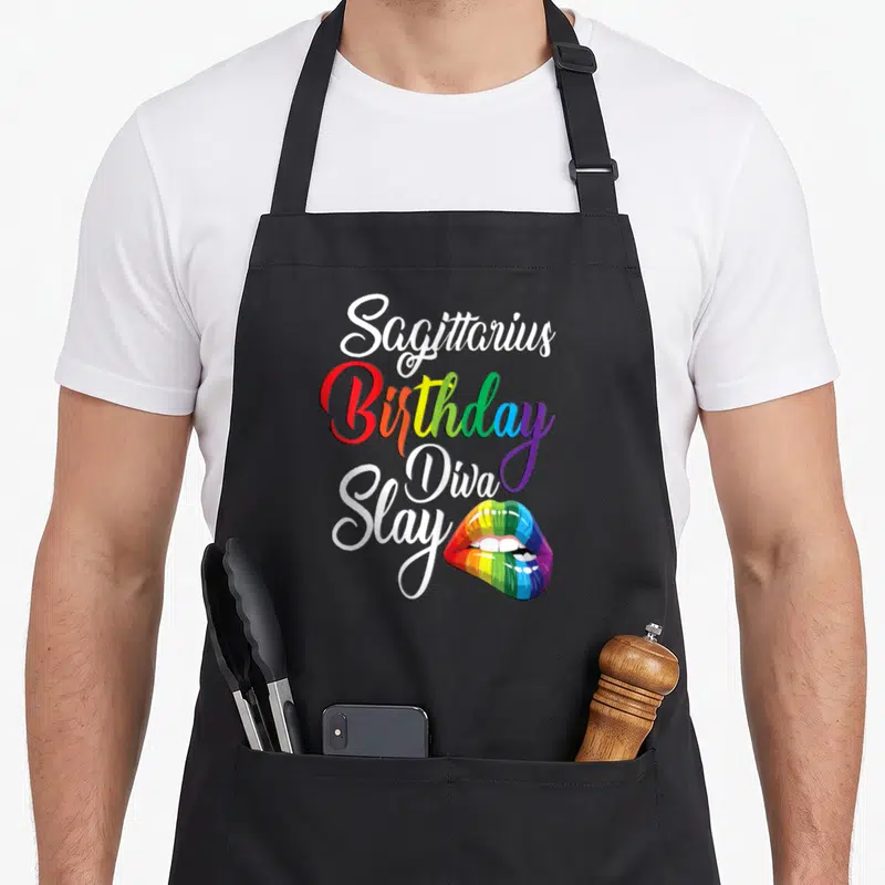 November rainbow apron - Sagittarius Birthday Diva Slay text with rainbow colored lips on black background — shown on a black cotton canvas apron against a white background