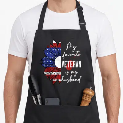 Sunflower best husband apron - Patriotic sunflower half-print with My favorite VETERAN is my husband text and red dog — shown on a black cotton canvas apron against a white background