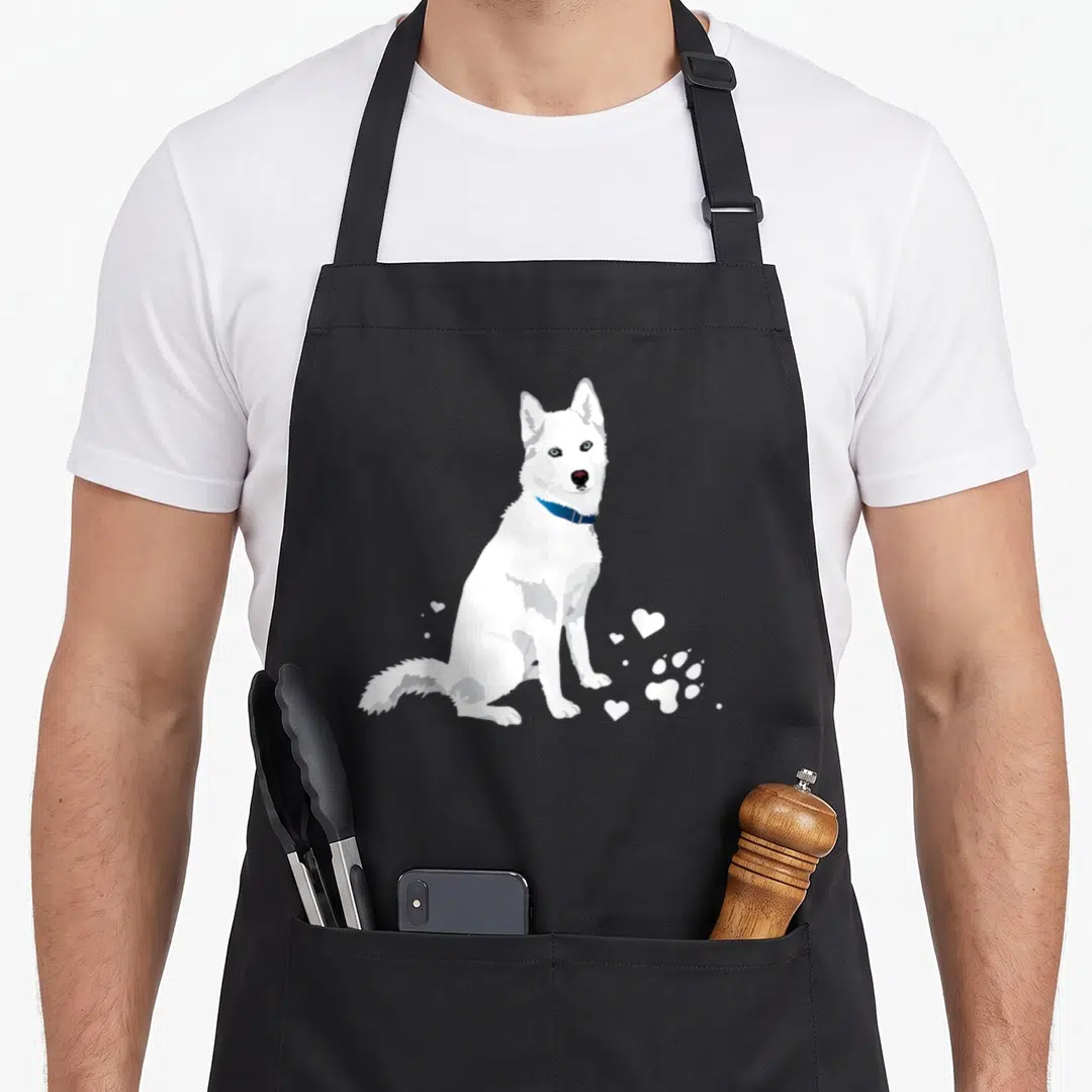 Sweet husky apron - White cartoon dog sitting with blue collar and white hearts paw print — shown on a black cotton canvas apron against a white background