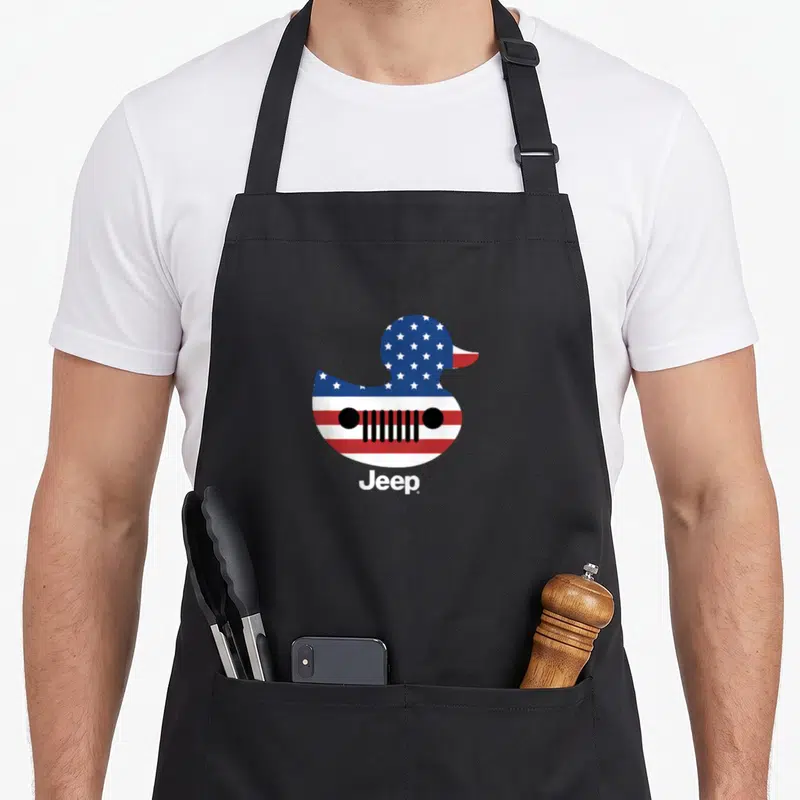 Flag duck apron - Rubber duck with US flag pattern and black jeep grille printed below — shown on a black cotton canvas apron against a white background