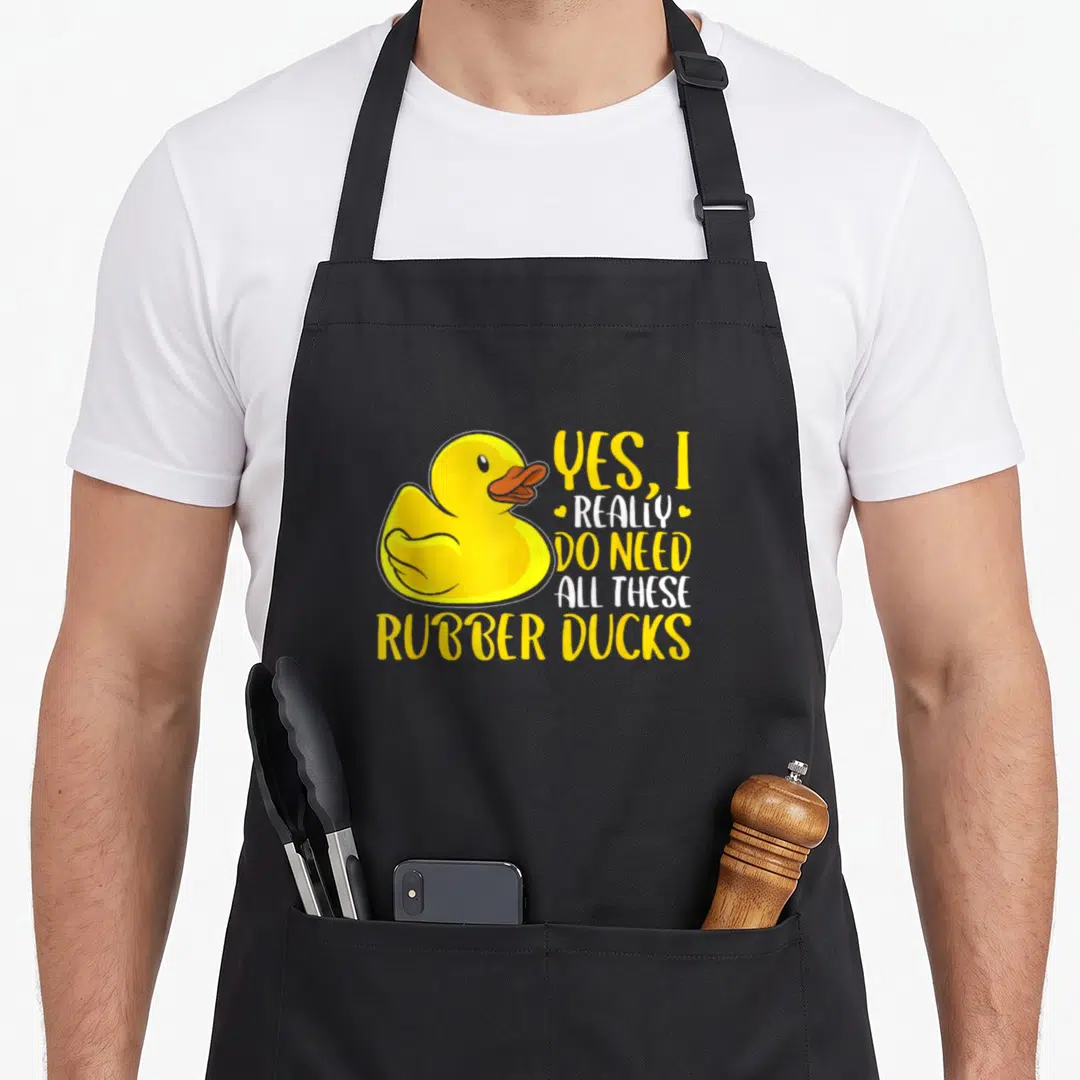 Rubber do i need an apron - Large yellow rubber duck with stacked text yes i really do need all these rubber ducks — shown on a black cotton canvas apron against a white background