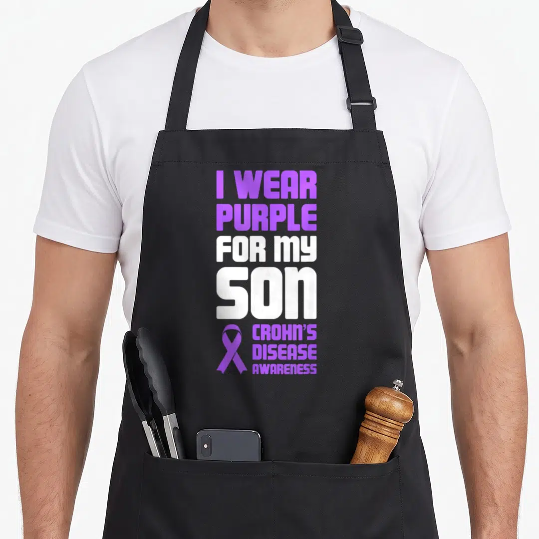 Son crohns awareness apron - Purple and white stacked text I WEAR PURPLE FOR MY SON CROHN'S DISEASE AWARENESS — shown on a black cotton canvas apron against a white background