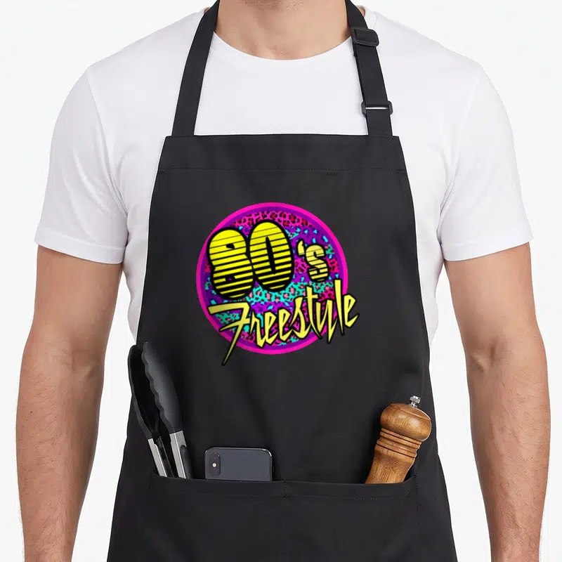 Dance 80s apron - 80's Freestyle text in striped yellow font inside pink circle with leopard print background — shown on a black cotton canvas apron against a white background