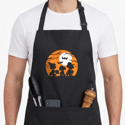 Treat silhouette halloween apron - Three grey children silhouettes against orange circle with white moon and grey bats — shown on a black cotton canvas apron against a white background