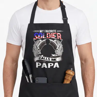 Soldier grandpa apron - Soldier silhouette with wings and rifles below flag text MY FAVORITE SOLDIER CALLS ME PAPA — shown on a black cotton canvas apron against a white background