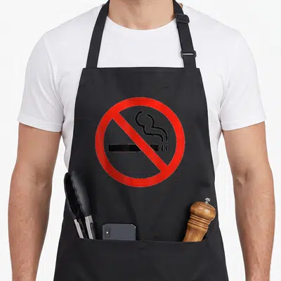 Symbol smoking apron - Red circle with diagonal slash over black cigarette and smoke lines — shown on a black cotton canvas apron against a white background