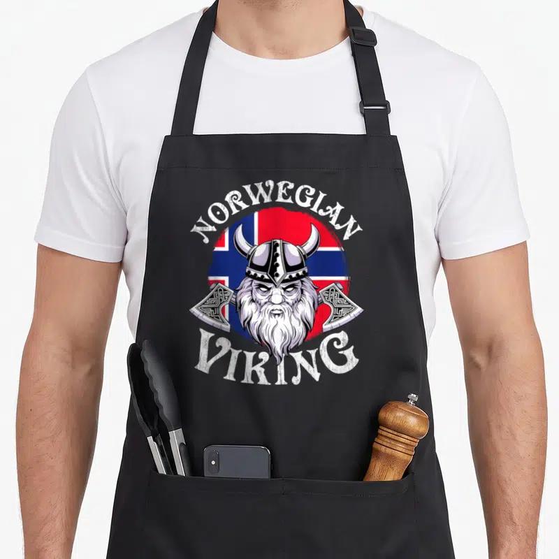 Viking norway norwegian kitchen aprons - Cartoon viking head over circular flag with two axes and white text — shown on a black cotton canvas apron against a white background