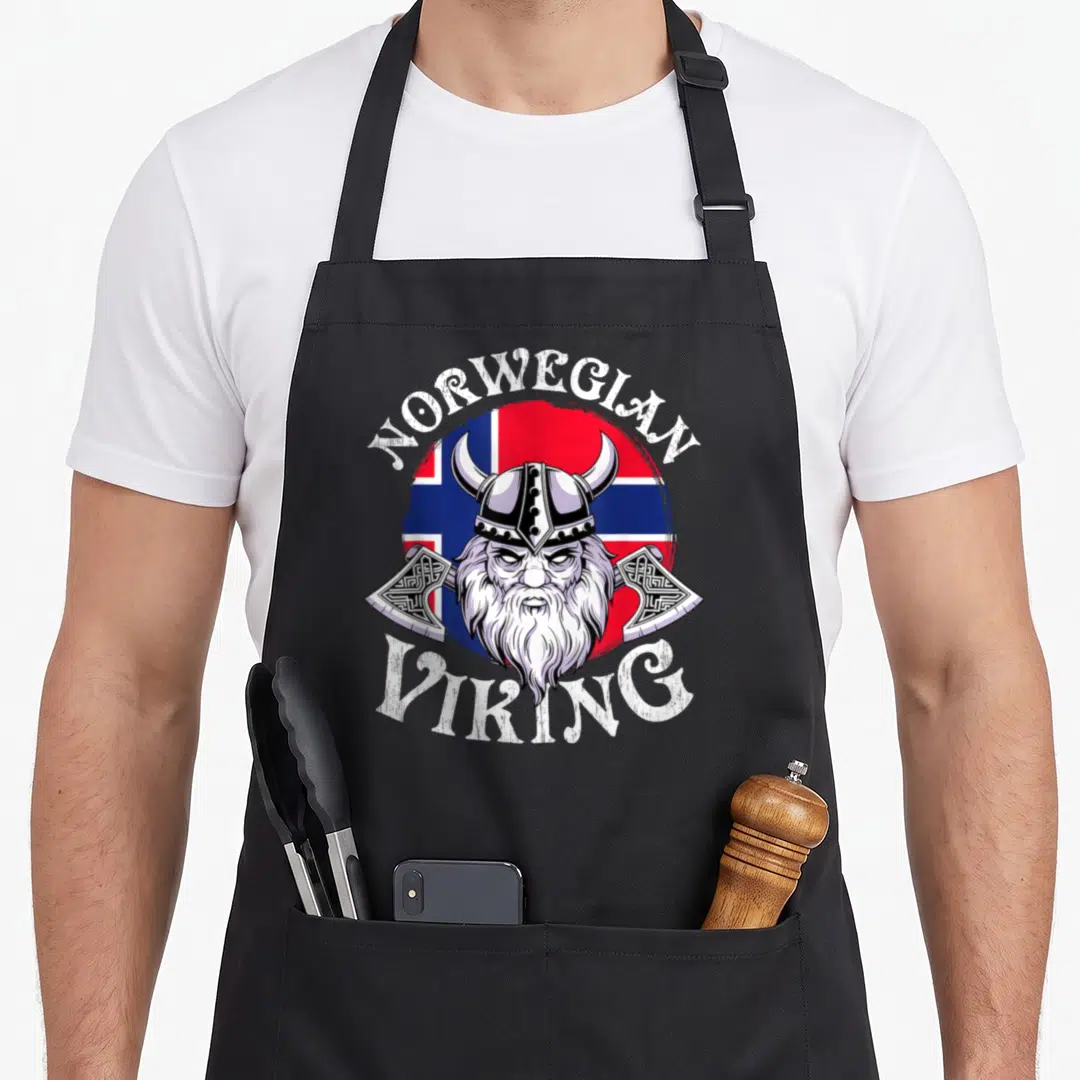 Viking norway norwegian kitchen aprons - Cartoon viking head over circular flag with two axes and white text — shown on a black cotton canvas apron against a white background