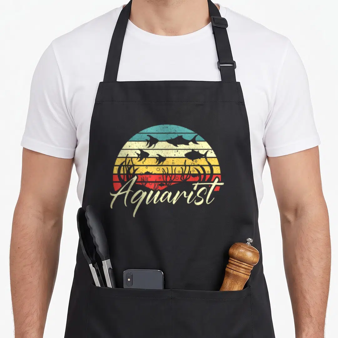 Aquarist fish apron - Retro semi-circle of colored stripes with fish silhouettes and script Aquarist text — shown on a black cotton canvas apron against a white background