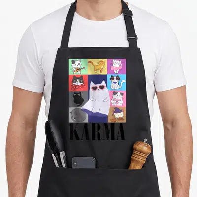 Music karma cat apron - Grid of cartoon cats with large white cat wearing heart glasses and black KARMA text below — shown on a black cotton canvas apron against a white background