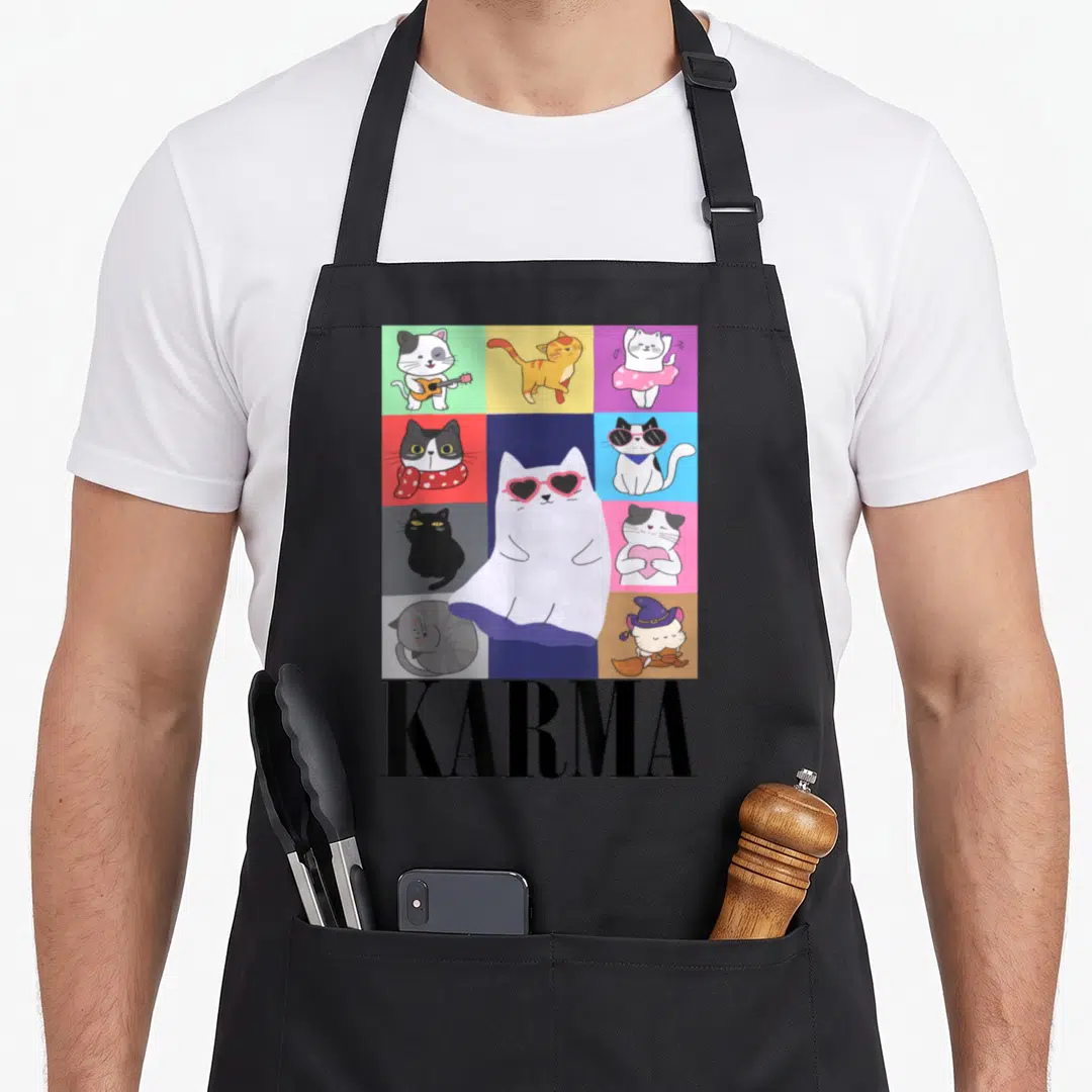 Music karma cat apron - Grid of cartoon cats with large white cat wearing heart glasses and black KARMA text below — shown on a black cotton canvas apron against a white background