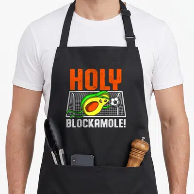 Blockamole avocado apron - Cartoon avocado goalie blocking soccer ball with holy blockamole text — shown on a black cotton canvas apron against a white background