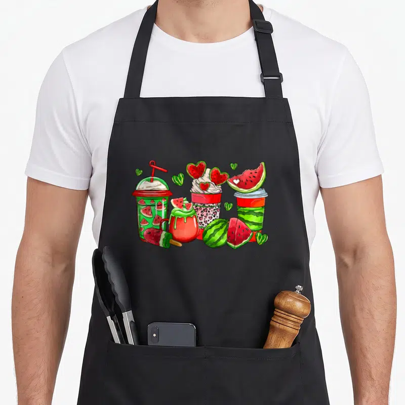 Cup coffee apron - Cartoon watermelon drinks, popsicle, and fruit slices in red green white pink — shown on a black cotton canvas apron against a white background
