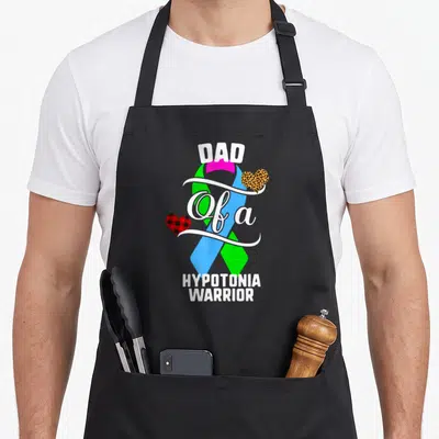 Hypotonia leopard apron - DAD Of a HYPOTONIA WARRIOR text with multi-color ribbon and leopard plaid hearts — shown on a black cotton canvas apron against a white background