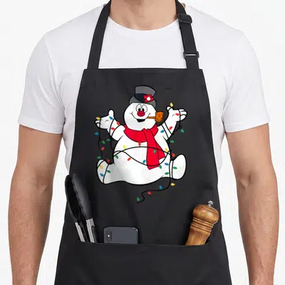 Frosty christmas snowman apron - White cartoon snowman with red scarf and multicolored lights wrapped around body — shown on a black cotton canvas apron against a white background