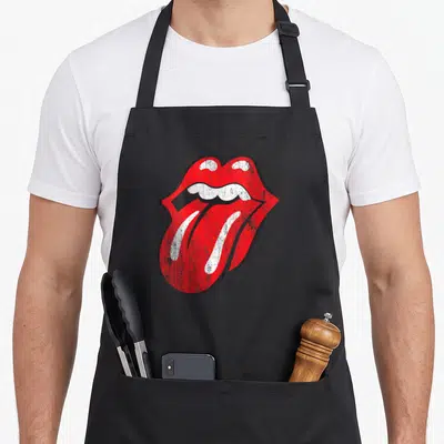 Funny distressed rolling stones apron - Red and white mouth graphic with tongue sticking out on black background — shown on a black cotton canvas apron against a white background