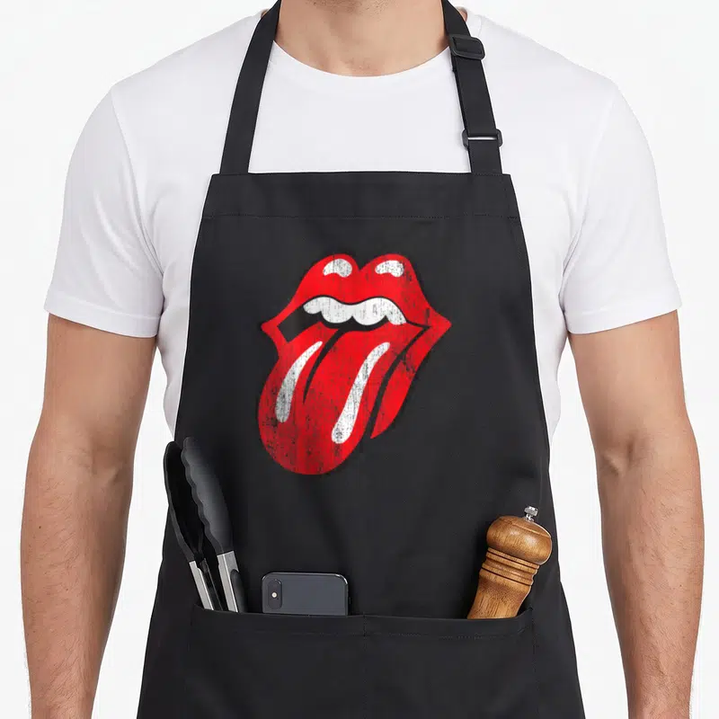 Funny distressed rolling stones apron - Red and white mouth graphic with tongue sticking out on black background — shown on a black cotton canvas apron against a white background