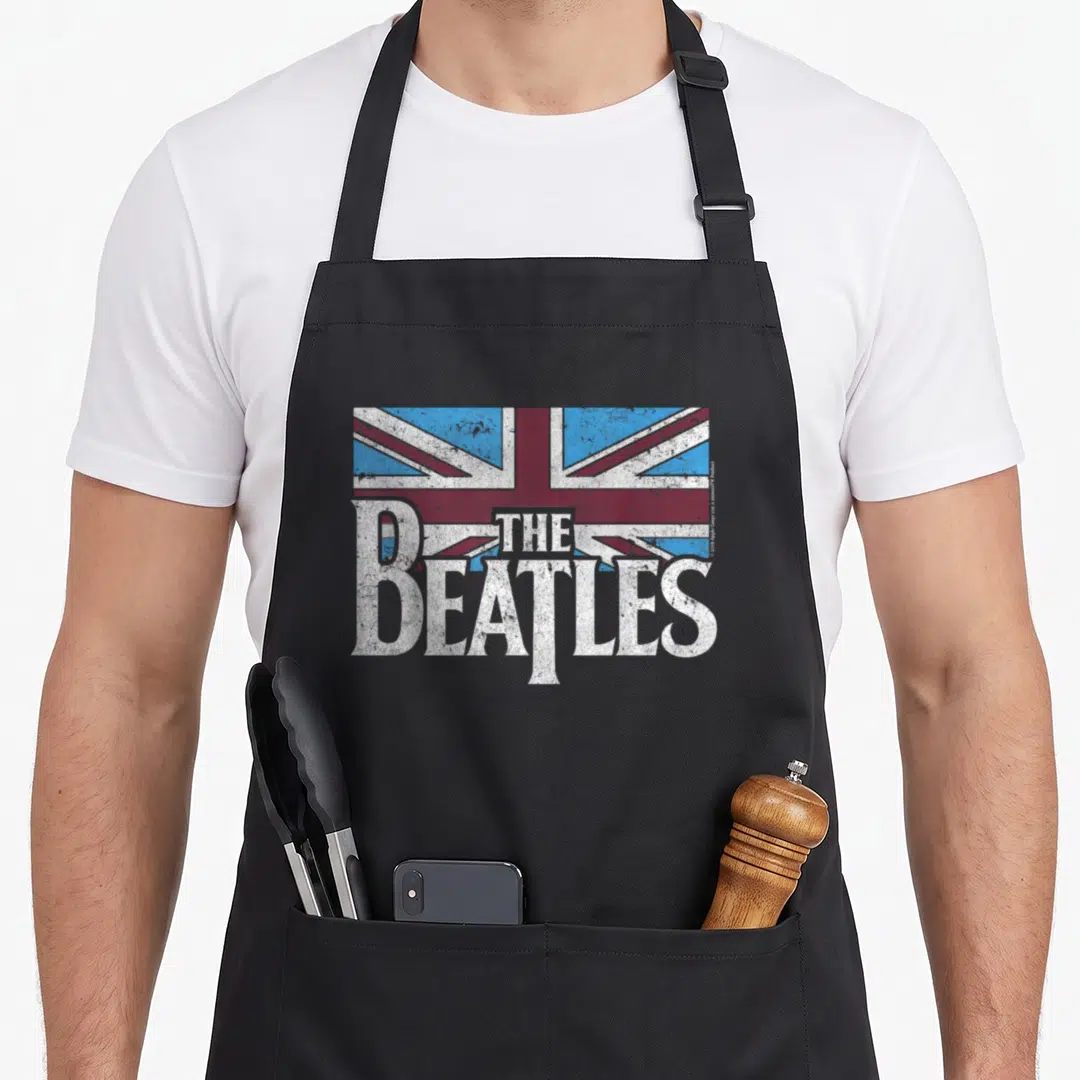 Flag blue apron - White The Beatles text over distressed red white and blue Union Jack flag — shown on a black cotton canvas apron against a white background