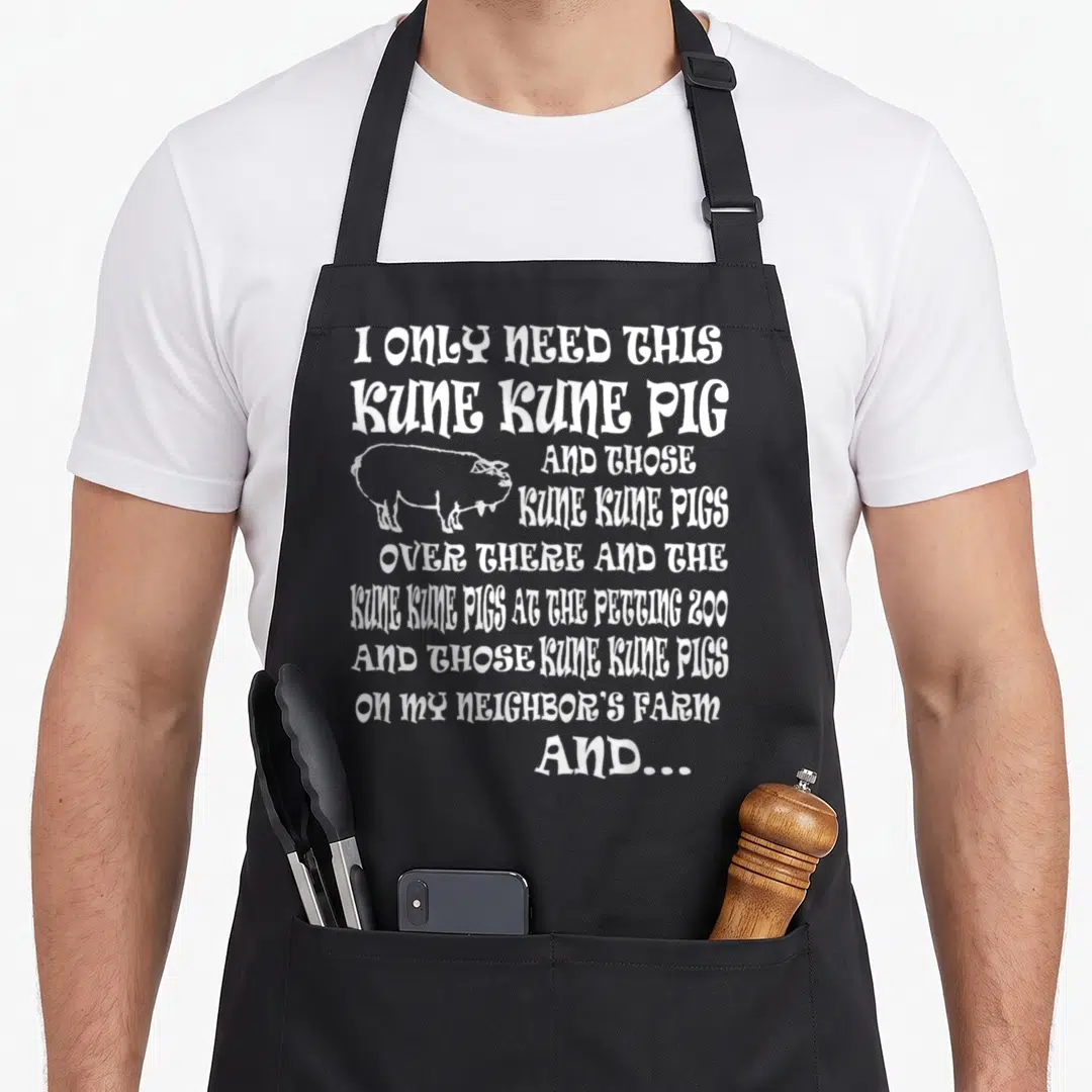 Kune pet apron - Stacked white text listing Kune Kune pigs next to a line drawing of a pig on a black background — shown on a black cotton canvas apron against a white background