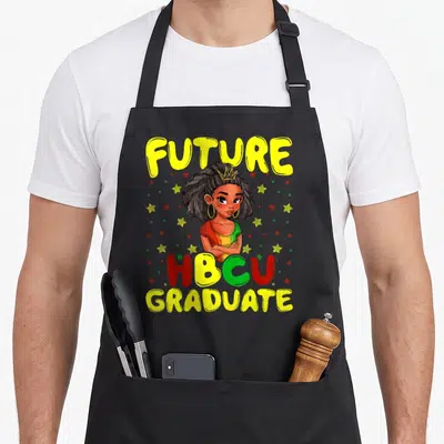 Grad grade girls apron - FUTURE HBCU GRADUATE text surrounding a crowned cartoon woman with yellow red and green stars — shown on a black cotton canvas apron against a white background