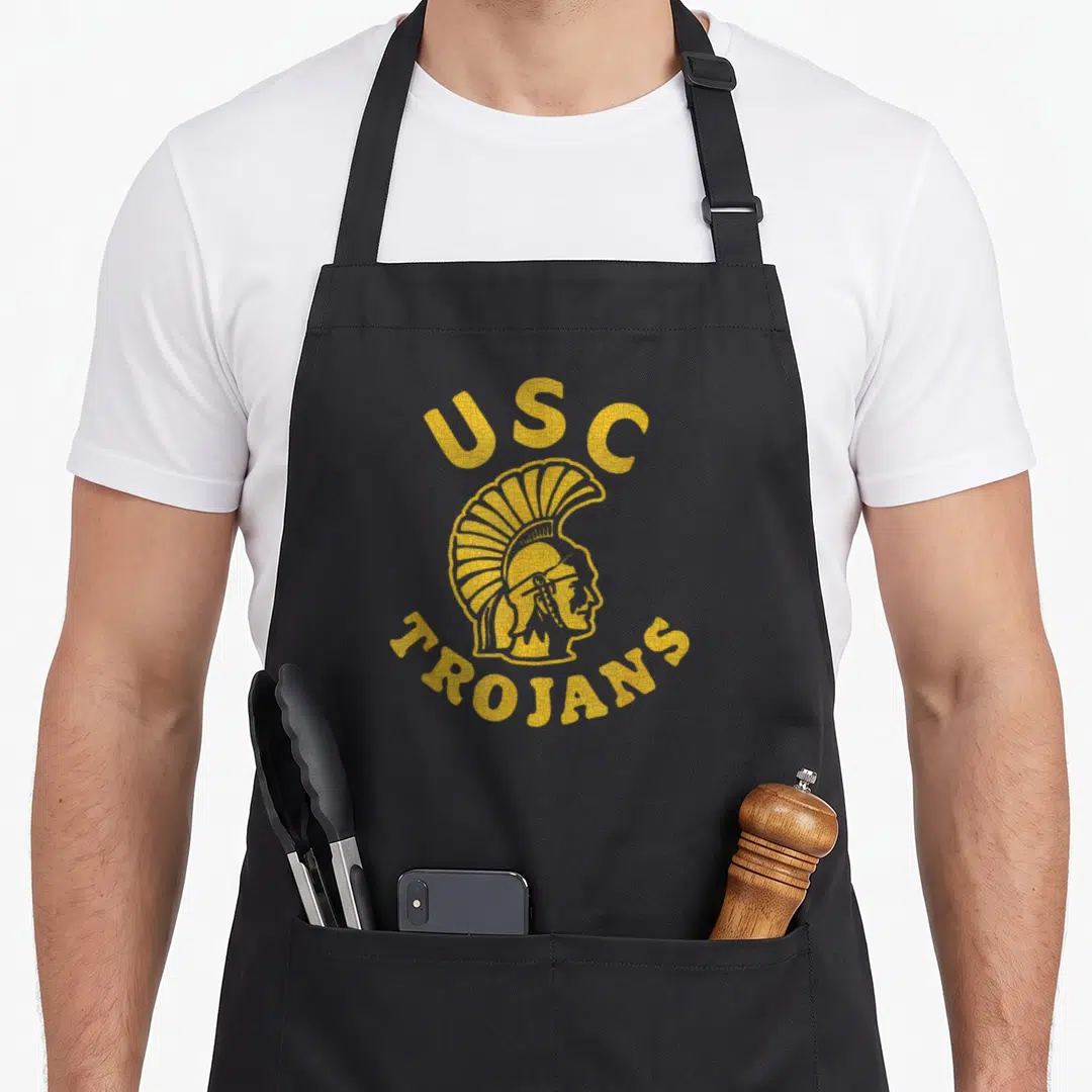 Tournament california apron - Yellow distressed Trojan helmet with arched USC TROJANS text — shown on a black cotton canvas apron against a white background