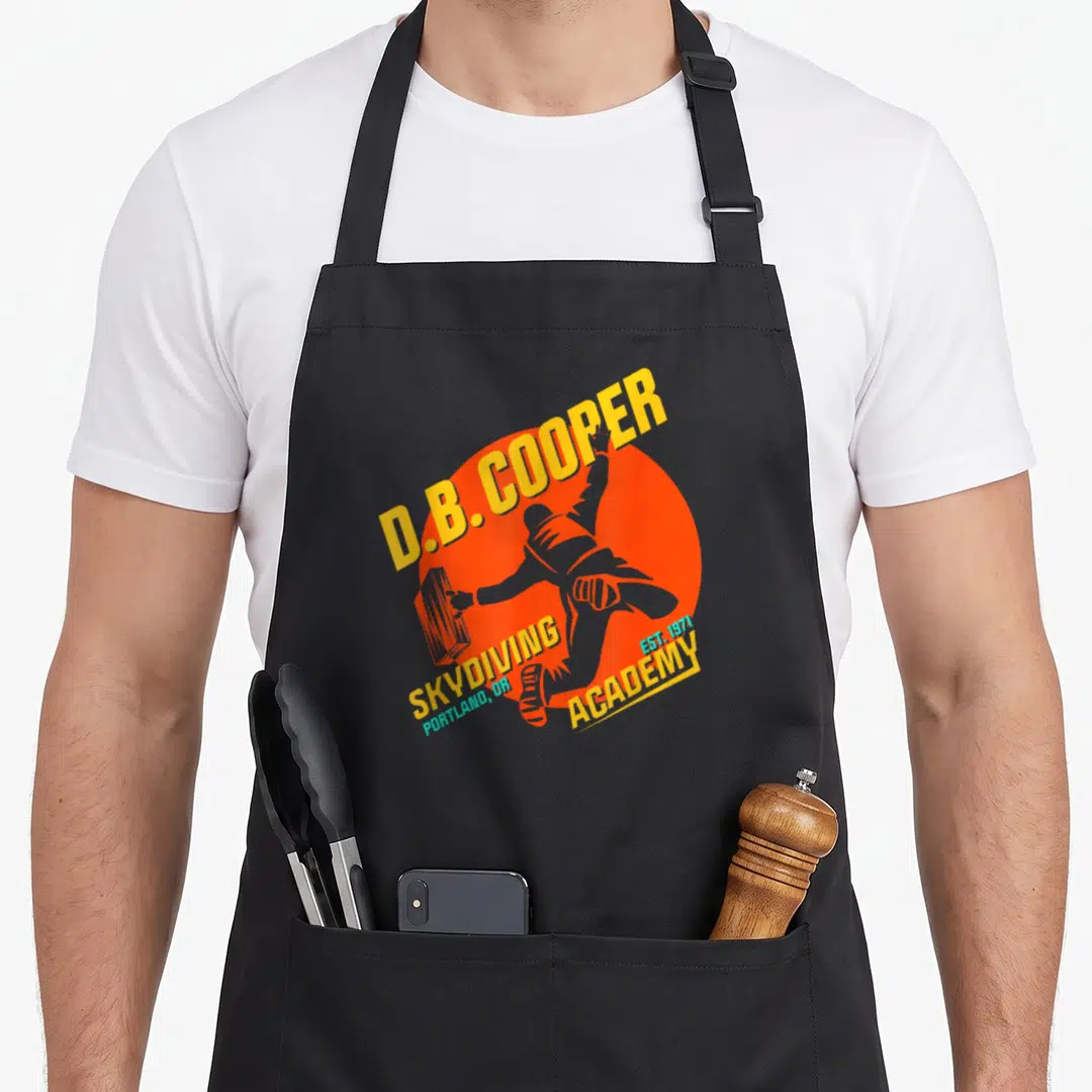 Academy skydiving apron - Retro D.B. Cooper skydiver holding suitcase inside orange circle with yellow and blue text — shown on a black cotton canvas apron against a white background