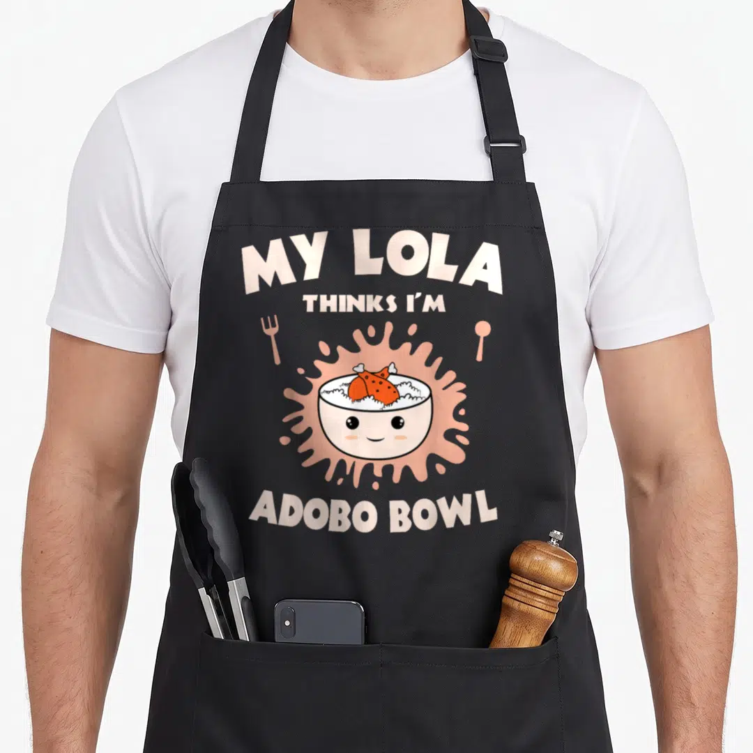 Adobo chicken apron - Cartoon rice bowl with face and adobo chicken on pink splatter with fork and spoon — shown on a black cotton canvas apron against a white background