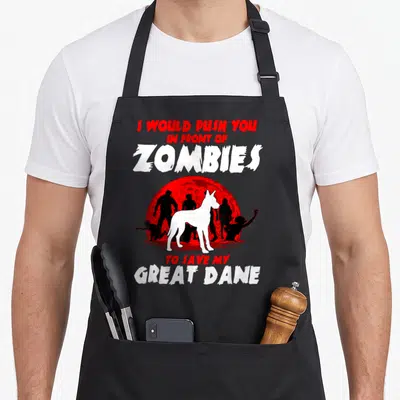 Zombie dog apron - Great Dane silhouette in front of red moon and black zombies with protective text — shown on a black cotton canvas apron against a white background