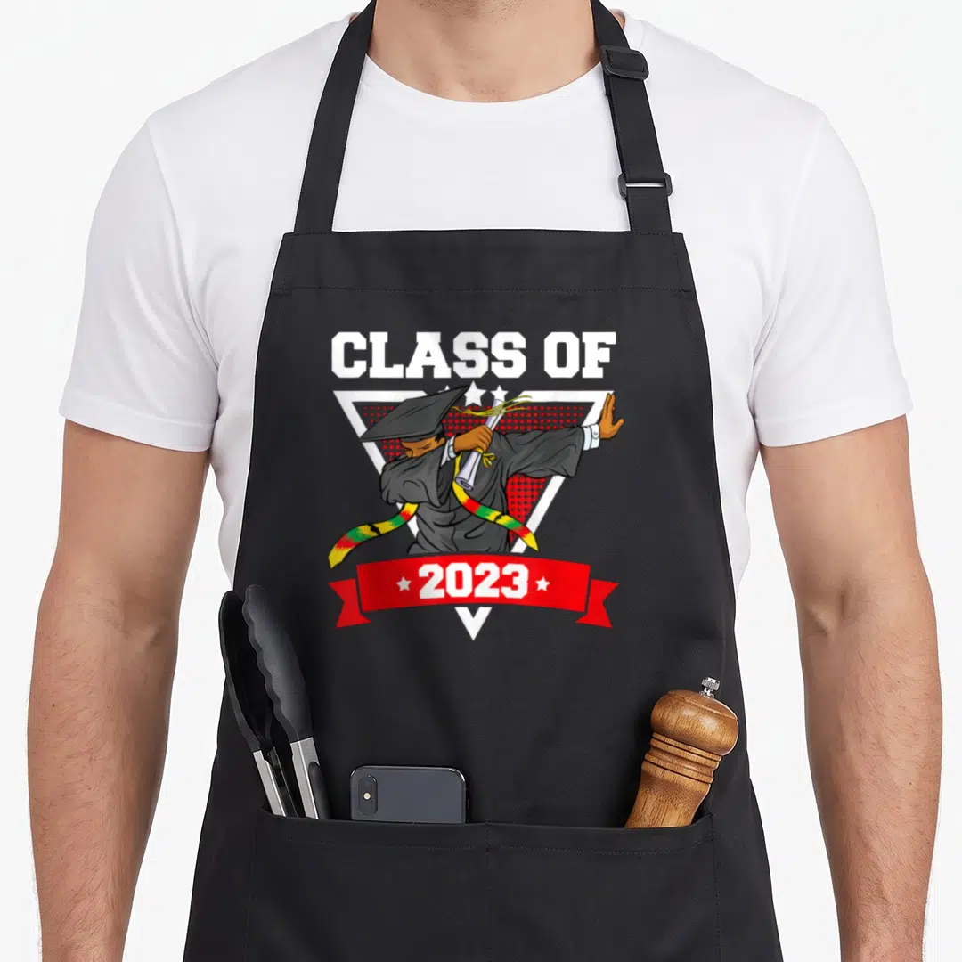 Dabbing history class apron - Cartoon grad dabbing in triangle with Class of 2023 text and colored stole — shown on a black cotton canvas apron against a white background