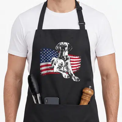 Vintage dane dog apron - Seated white grey dog in front of distressed red white blue USA flag — shown on a black cotton canvas apron against a white background