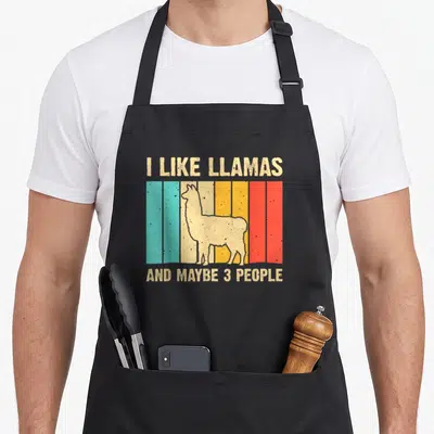 Farming alpaca apron - I like llamas and maybe 3 people text with llama silhouette over five colored stripes — shown on a black cotton canvas apron against a white background