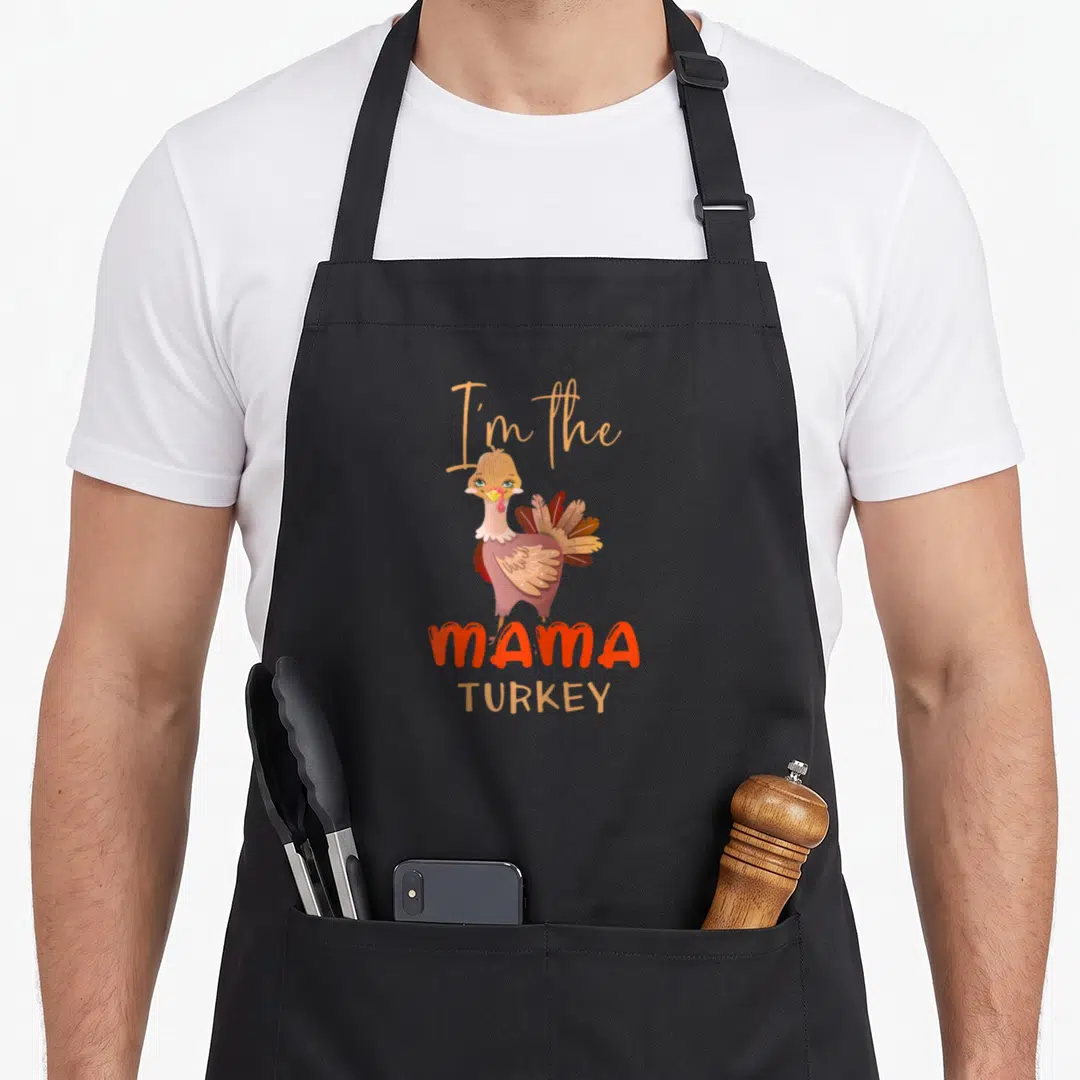 Mama funny turkey apron - Cartoon turkey with I'm the MAMA TURKEY text in brown and orange — shown on a black cotton canvas apron against a white background