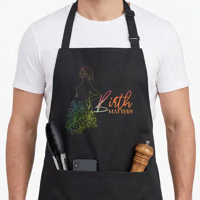 Labour nurse apron - Rainbow line-art pregnant woman silhouette with sunflowers and Birth MATTERS text — shown on a black cotton canvas apron against a white background