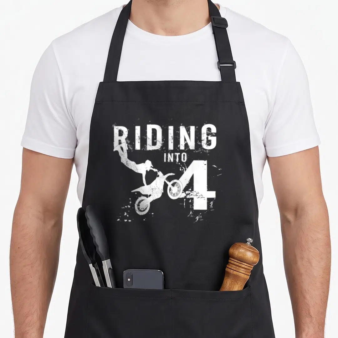 Riding 4th birthday apron - White distressed dirt bike rider jumping near the number 4 text — shown on a black cotton canvas apron against a white background