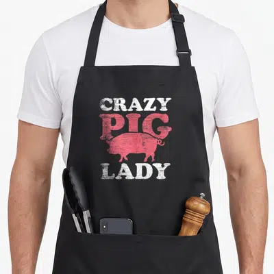 Funny crazy pig man apron - Distressed white and pink text reading CRAZY PIG LADY with a pig silhouette — shown on a black cotton canvas apron against a white background