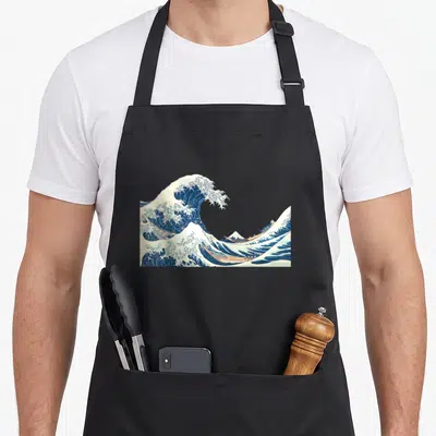 Katsushika wave apron - Blue and white wave with three tan boats and a small mountain in realistic Japanese style — shown on a black cotton canvas apron against a white background