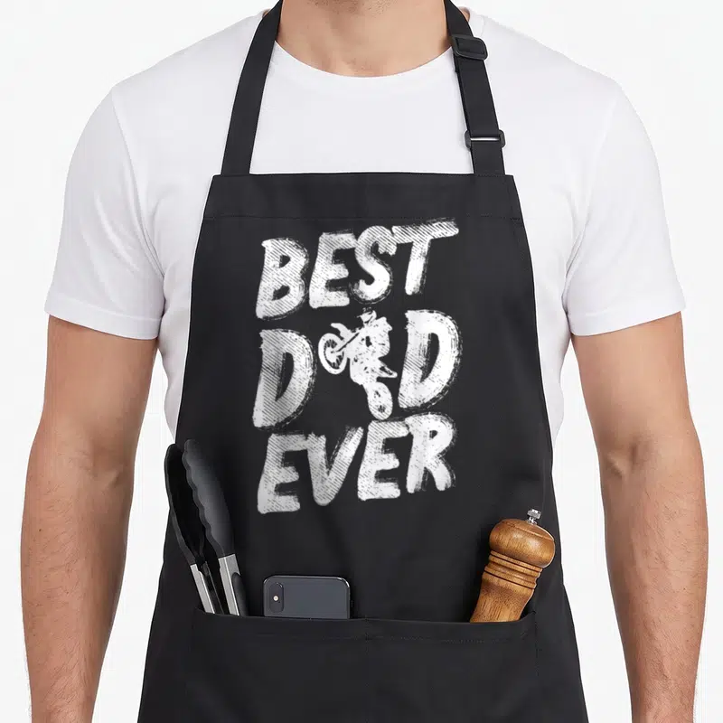 Dirt bike motorcycle aprons - White distressed text reading Best Dad Ever with a central dirt bike rider silhouette — shown on a black cotton canvas apron against a white background