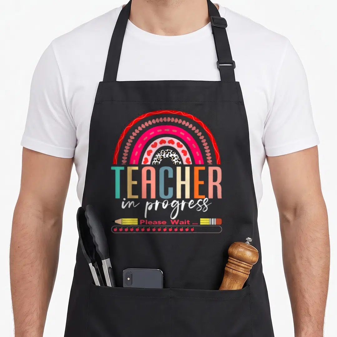 Future progress wait teacher apron - Rainbow with TEACHER in progress text, pencil, eraser, and apple loading bar — shown on a black cotton canvas apron against a white background