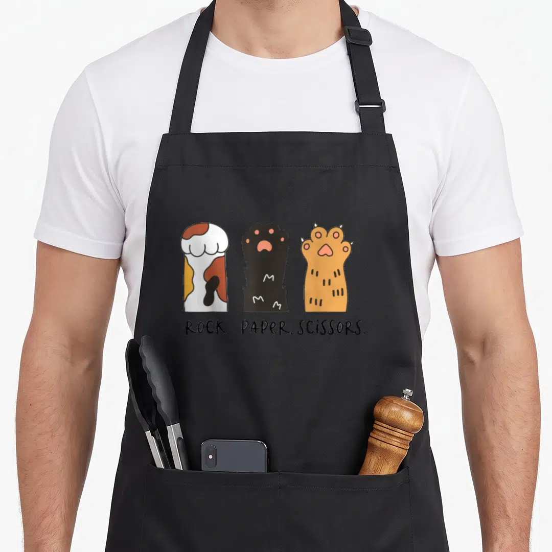 Toddler paper apron - Three cartoon cat paws in calico black and orange above rock paper scissors text — shown on a black cotton canvas apron against a white background