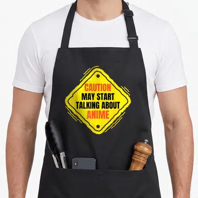Talking anime apron - Yellow diamond caution sign with red and black text reading CAUTION MAY START TALKING ABOUT ANIME — shown on a black cotton canvas apron against a white background
