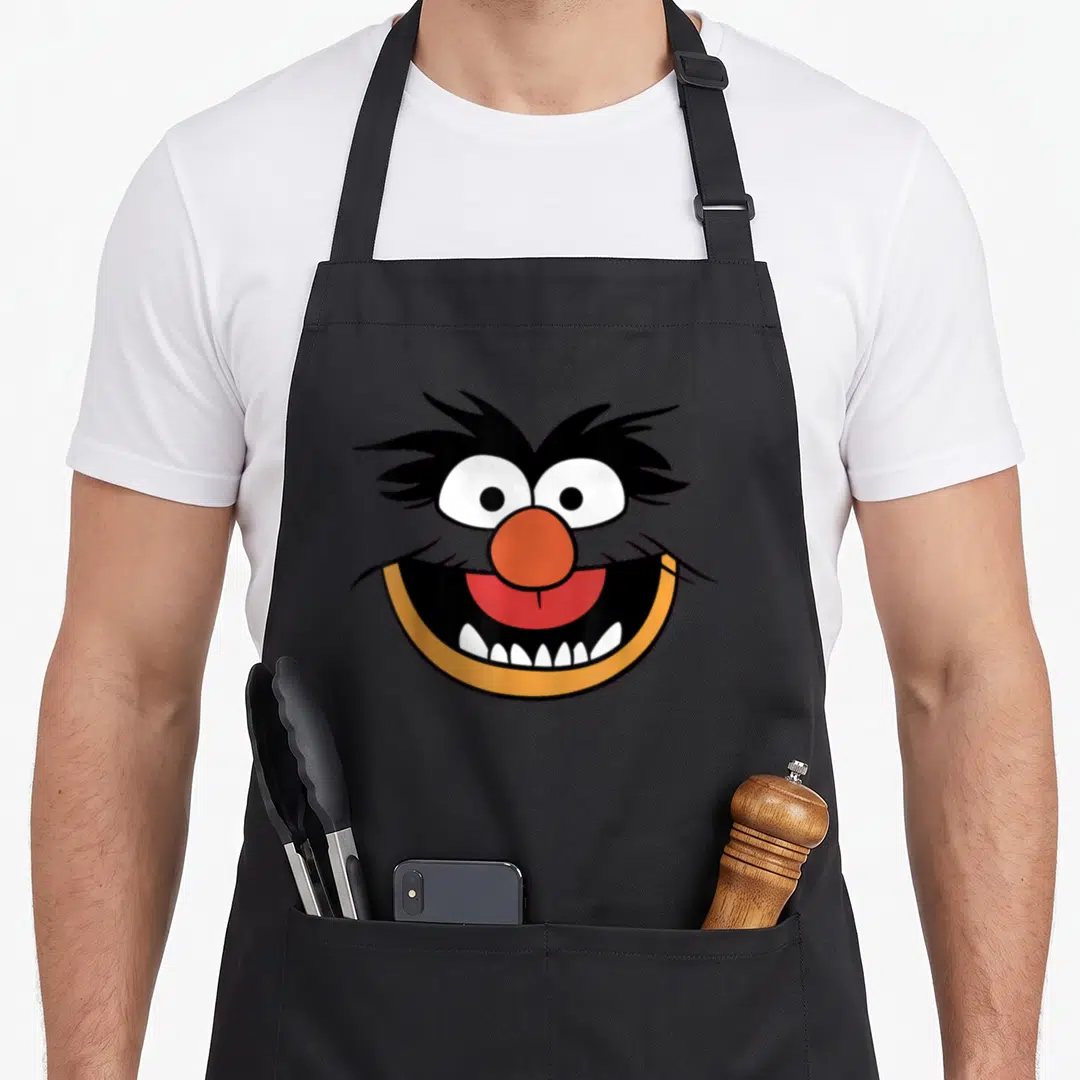 Face animal apron - Cartoon face with orange nose, black fur, white eyes, and red mouth — shown on a black cotton canvas apron against a white background